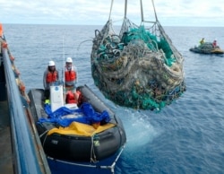 FILE - In this April 11, 2021, photo provided by Matt Saunter, Joao Garriques, left, and Matthew Chauvin load fishing nets onto a ship near Kure Atoll in the Northwestern Hawaiian Islands.