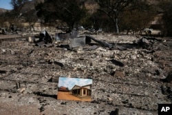A photo of what the area looked like before is placed on the remains of a building leveled in the Woolsey Fire at decimated Paramount Ranch, during U.S. Interior Secretary Ryan Zinke's visit to the ranch, Nov. 15, 2018, in Agoura Hills, Calif.