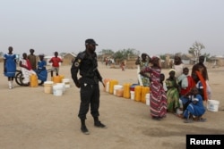 FILE - A Cameroonian police officer stands next to people waiting for water at the Minawao refugee camp for Nigerians who fled Boko Haram attacks in Minawao, Cameroon, March 15, 2016.