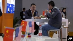 Visitors chat near American and Chinese flags displayed at a booth at the China International Import Expo in Shanghai, Nov. 6, 2019. Washington and Beijing have agreed to cancel tariff hikes as their trade negotiations progress.