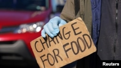 FILE - Holding a sign, a jobless man panhandles at an intersection in Falls Church, Virginia, April 3, 2020. 