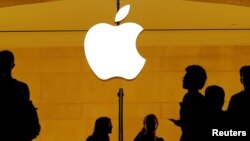 FILE - Customers walk past an Apple logo inside of an Apple store at Grand Central Station in New York, Aug. 1, 2018.