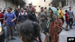 A Palestinian woman covered in dust and dirt carries a child, as raging battles between Israel and the Hamas movement continue for the sixth consecutive day Gaza City on Oct. 12, 2023.