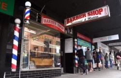 Men queue for a haircut outside a barber shop in Melbourne on October 19, 2020, as some of the city's three-month-old stay-at-home restrictions due to the COVID-19 coronavirus outbreak were further eased on falling infection rates.