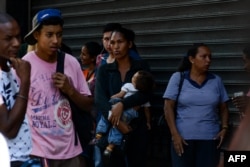 A woman holds her baby while queuing outside a supermarket in Caracas to buy basic food and household items, Nov. 10, 2017. In crisis-stricken Venezuela, the cost of the basic basket of goods soared to nearly 2.7 million bolivars in September, the equivalent of six minimum monthly wages.