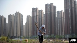 资料照：安徽省合肥一处新开发的楼盘旁，一名妇女在一小块田地里劳作。（2011年5月21日）