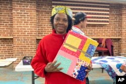 Hadijah Petro, who is originally from Congo, shows a handmade quilt she picked out for herself at a blanket giveaway for refugees and immigrants on March 21, 2023, in Burlington, Vt. Each included a note from the crafter about her or his own family history of immigration or migration. (AP Photo/Lisa Rathke)