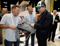 Colorado Gov. Jared Polis, right, looks over a pack made of hemp with Rob Bondurant, left, and Mark Galbraith of Osprey Packs of Cortez, Colorado, in the company's exhibit at the Outdoor Retailer Summer Market in Denver, Colorado, June 19, 2019.