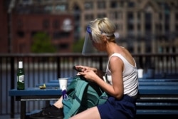 A woman wearing a protective shield looks at her phone as the lockdown because of the coronavirus outbreak continues, in London, May 8, 2020.