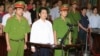 Cu Huy Ha Vu (C) stands between policemen in the dock during his trial at a court in Hanoi, August 21, 2011.
