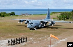 FILE - Philippine troops march as a Philippine Air Force C-130 transport plane carrying Philippine Defense Secretary Delfin Lorenzana, Armed Forces Chief Gen. Eduardo Ano and other officials, sits on the tarmac at the Philippine-claimed Thitu Island.