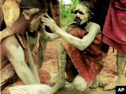 An Ogiek paints his fellow warrior's face