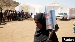 A woman carries a tin of food aid distributed by the WFP, at the Um Rakuba refugee camp which houses Ethiopians fleeing the fighting in the Tigray region, on the the border in Sudan, Dec. 3, 2020.