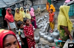 FILE - Rohingya women and children wait in a queue to collect water at the Leda camp, an unregistered camp for Rohingya in Teknaf, Bangladesh.