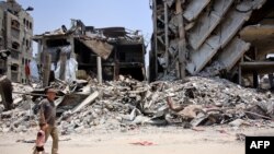 Палестинец држи за рака мало момче додека поминува покрај урнатините на уништените згради во бегалскиот камп Џабалија, во северниот дел на Појасот Газа на 3 јуни 2024 година.