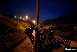 FILE - Migrants from Honduras, part of a caravan of thousands from Central America trying to reach the United States, jump the fence to cross it illegally into San Diego County, U.S., taken from the border wall in Tijuana, Mexico, at right, Jan. 16, 2019.