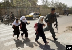 FILE - An Afghan policeman walks with school girls across the road in Herat, west of Kabul, Afghanistan, March 16, 2010.
