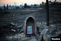 FILE - A religious image rests front of debris of an immigrant's shack after an accidental fire in Santiago, Chile, Dec. 14, 2016.