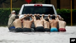 People push a stalled pickup through a flooded street in Houston, after Tropical Storm Harvey dumped heavy rains, Aug. 27, 2017.