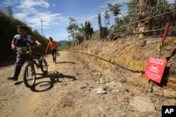 FILE - Boys walk past a farm marked with tape and signs warning of land mines in Cocorna, Colombia, June 25, 2015.