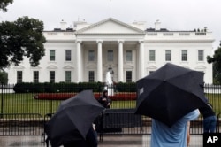 People stand on Pennsylvania Avenue as rain falls at the White House, July 28, 2017, in Washington. Rarely has the gap between the priorities of a president and lawmakers in his own party been so stark in the nation's capital.