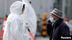 Workers in protective gear escort disembarking passengers from the coronavirus-hit Diamond Princess cruise ship docked at Yokohama Port, south of Tokyo, Feb. 20, 2020.