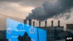 FILE - Pedestrians and an electronic screen displaying COVID-19 prevention advice is reflected in a glass wall as smog billows from a factory in Moscow, Dec. 3, 2020.