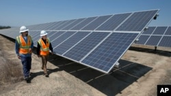 FILE - Employees walk past solar panels at a plant in Dixon, California, Aug. 17, 2017.