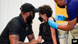 A father, left, comforts his son as he is inoculated with his first dose of a COVID-19 vaccine for children five to 12 years, at Public School 19 in the East Village neighborhood of New York City, Nov. 8, 2021. 