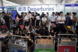 Airport security personnel stand guard as travelers walk past protesters holding a sit-in rally at the departure gate of the Hong Kong International Airport in Hong Kong, Aug. 13, 2019.