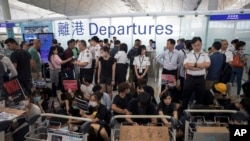 Airport security personnel stand guard as travelers walk past protesters holding a sit-in rally at the departure gate of the Hong Kong International Airport in Hong Kong, Aug. 13, 2019. 