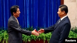 FILE - Japan's Prime Minister Shinzo Abe shakes hands with China's President Xi Jinping (R) during their meeting at the Great Hall of the People, on the sidelines of the Asia Pacific Economic Cooperation (APEC) meetings, in Beijing, Nov. 10, 2014. 