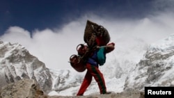 FILE - A Nepalese porter walks with his load from Everest base camp in Nepal, May 2011. Porters walk for weeks, sometimes carrying supplies heavier than their own body weight.