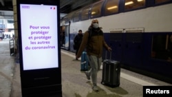 A man wearing a protective face mask walks past an announcement for travelers to protect themselves and others from the coronavirus, at Montparnasse train station in Paris, France, March 13, 2020.