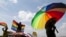 FILE - A person holds an umbrella bearing the colors of the rainbow flag as others wave flags during a gay pride rally in Entebbe, Uganda, Aug. 9, 2014. A crowd in Ghana tore down a billboard promoting LGBTQ tolerance in June 2022, during Pride month.
