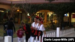 In this Feb. 8, 2020, photo, two women wearing traditional Mexican dresses walk by during the celebration of the town's 45th year since it was incorporated in Guadalupe, Ariz.