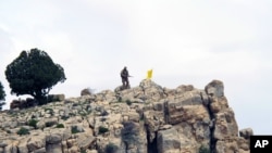 FILE - A Hezbollah fighter stands on a hill next to the group's yellow flag at Assal al-Ward, Syria, May 9, 2015. Experts say Iran's sending Afghan refugees to fight on the Syrian front, alongside Hezbollah and Iranian forces, has long-term implications for Afghanistan and the region at large.