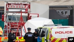 FILE - Police officers are on the scene after a truck, in rear, was found to contain 39 dead bodies, in Thurrock, England, Oct. 23, 2019. 