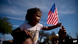 A migrant girl with a U.S. flag sits on the shoulders of a man marching with other migrants to the Chaparral border crossing in Tijuana, Mexico, Sunday, Nov. 25, 2018, as they try to reach the U.S.