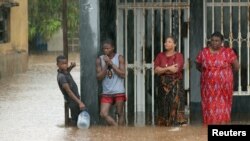 Residents stand outside a flooded house as rain falls in the aftermath of Cyclone Kenneth in Pemba, Mozambique, Apr. 28, 2019.