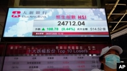 A woman wearing a face mask stands beneath a bank's electronic board showing the Hong Kong share index at Hong Kong Stock Exchange in Hong Kong, July 28, 2020. 