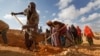 In this photo taken Wednesday, March 8, 2017, men dig with shovels and women take away the earth to build a dam so that if rains do come the water can be stored near Bandar Beyla in Somalia's semiautonomous northeastern state of Puntland.