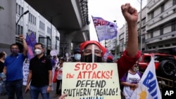 A woman, clenching her fist, holds a sign condemning recent government raids on activists, during a rally near the Malacanang presidential palace, in Manila, Philippines, March 8, 2021.