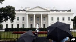 People stand on Pennsylvania Avenue as rain falls at the White House, July 28, 2017, in Washington. Rarely has the gap between the priorities of a president and lawmakers in his own party been so stark in the nation's capital. 