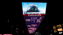 An outdoor screen depicts a Chinese fighter jet pilot giving a thumbs up in the recently concluded Joint Sword exercise around Taiwan during the evening news broadcast in Beijing, April 10, 2023