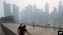 FILE - A worker wears a mask as he helps another push equipment during a hazy day in Singapore, Thursday, Sept. 10, 2015. 