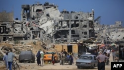 দক্ষিণ গাজার খান ইউনিসে বিধ্বস্ত ভবনের পাশ দিয়ে ফিলিস্তিনিরা হেঁটে যাচ্ছেন। ফটোঃ ৩০ জুন, ২০২৪।