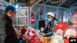This photo taken Dec. 24, 2020, shows a vendor offering drinks to a customer at a Christmas-themed market outside of a shopping mall complex on Christmas Eve in Shanghai. 