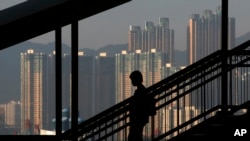 FILE - A woman walks down a stairway against the backdrop of high-rise apartment buildings in Hong Kong. 