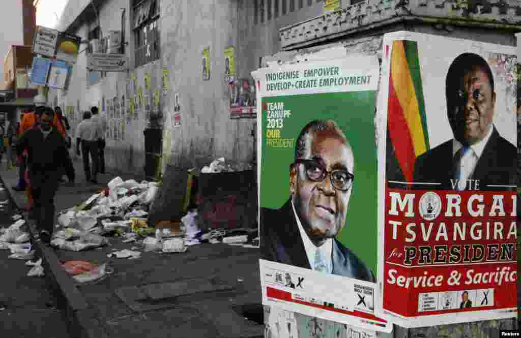 Election campaign posters are pictured near Zimbabweans walking on a street blocked by uncollected garbage in Harare July 17, 2013. President Robert Mugabe's rivals said the chaotic organisation of early voting for soldiers and police showed Zimbabwe was not ready for the July 31 general election in which nearly six million people had registered to vote.